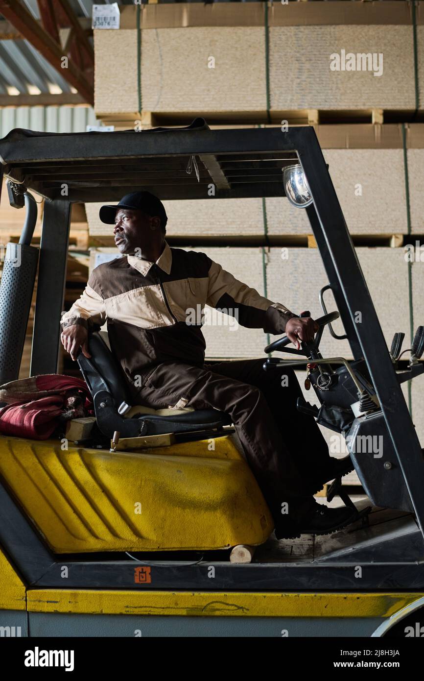 African forklift driver sitting in loader and driving during work at industrial factory Stock Photo