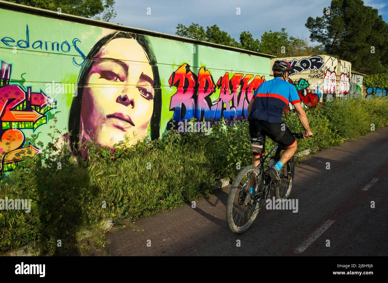 Granada, Andalusia, Spain : A cyclist on the bikeway cycles past graffiti mural by street artist El niño de las pinturas. Stock Photo
