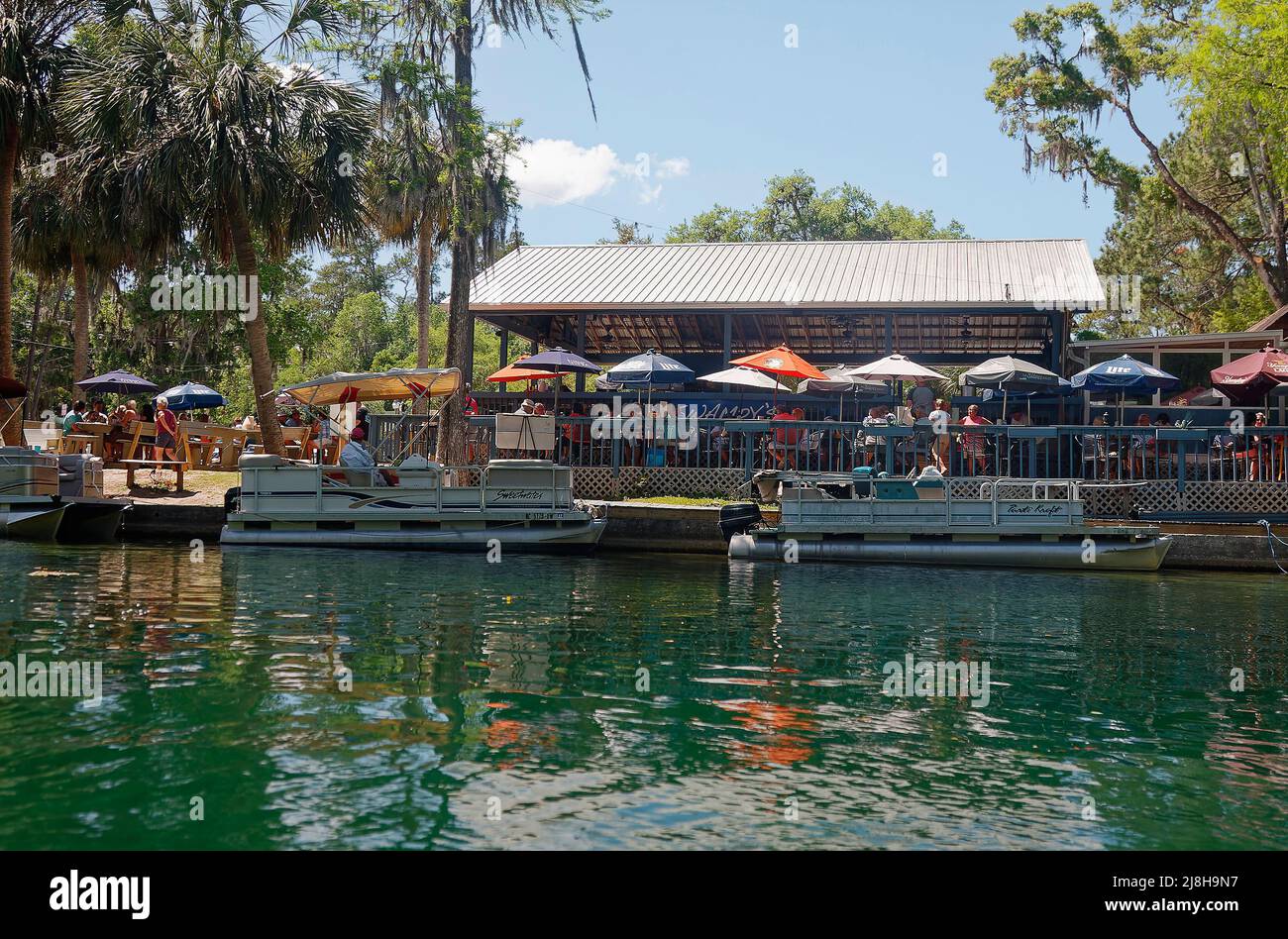 riverside restaurant, outdoor eating, pontoon boats docked, umbrellas, people, recreation, water, Rainbow River, Florida, Dunnellon, FL Stock Photo