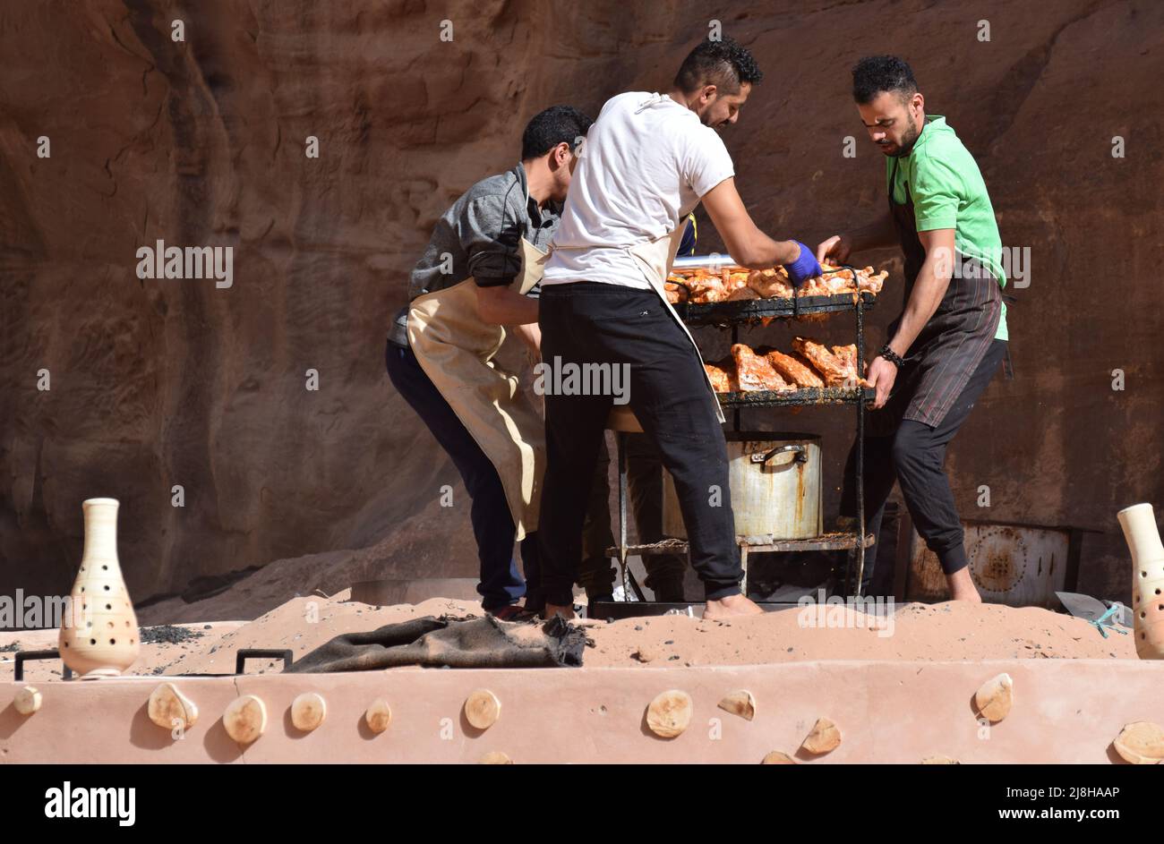 3 men carrying a rack of meat and vegetables to be barbecued underground. This traditional Jordanian way of cooking is know as ‘zarb’ Stock Photo