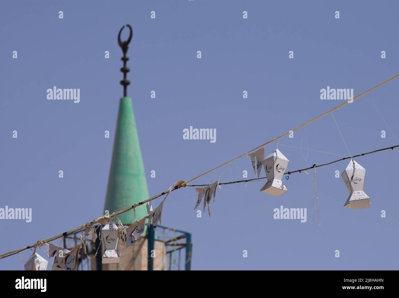 Hanging Ramadan lantern street decorations with the minaret of a mosque in the background against a blue sky in Jordan in the Middle East Stock Photo