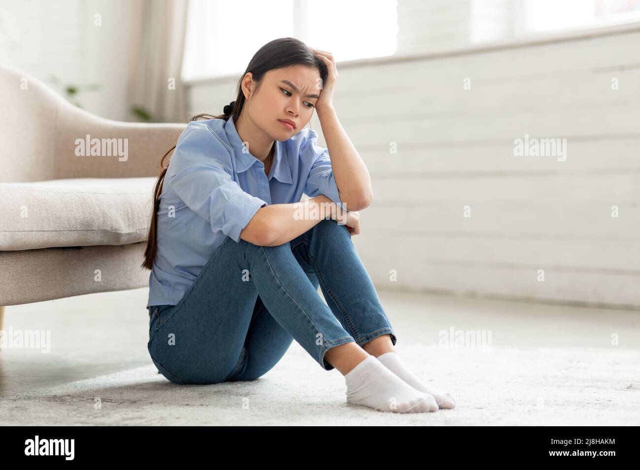 Frustrated korean woman sitting on floor at home Stock Photo