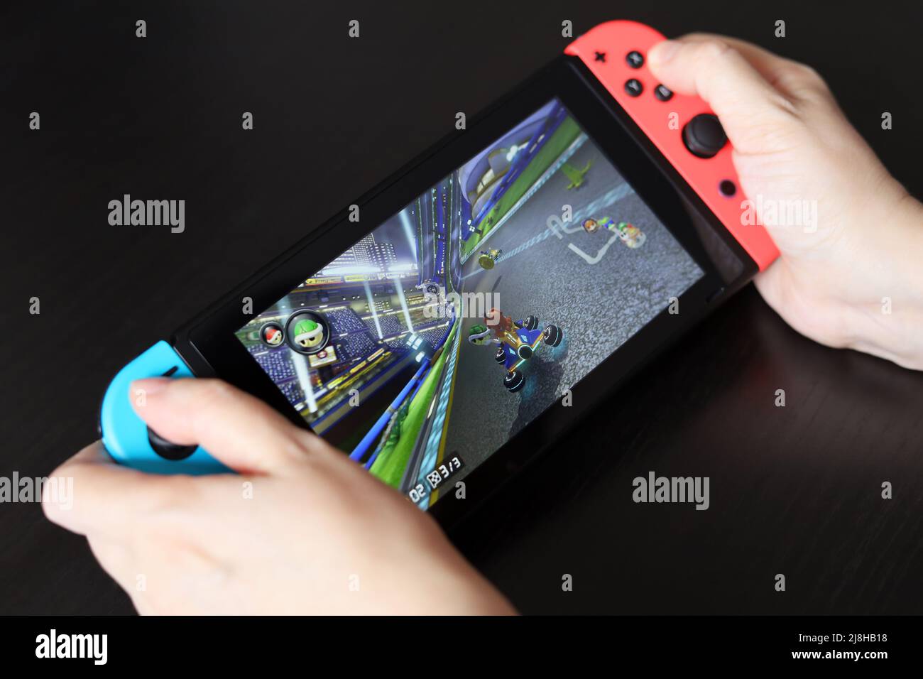 Girl playing Mario Kart 8 game on Nintendo Switch console in handheld mode, selective focus on a screen Stock Photo