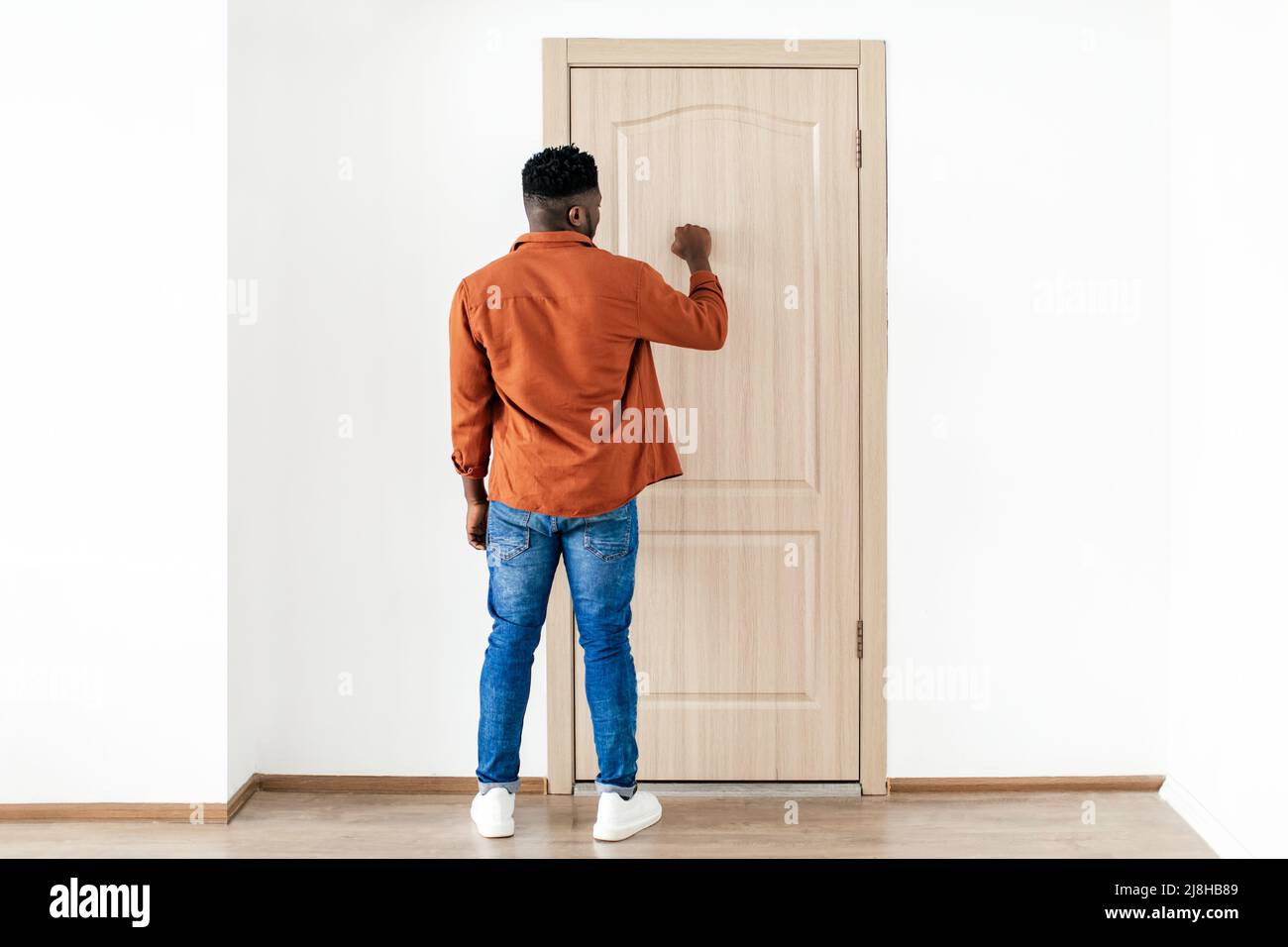 Black Male Knocking At Door Standing Back To Camera Indoors Stock Photo