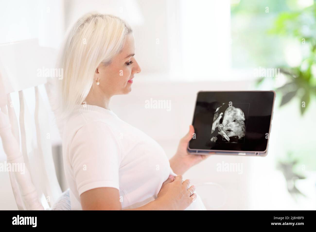 Pregnant woman at home. Young expecting mother looking at ultrasound picture on tablet computer. Healthy pregnancy. Stock Photo