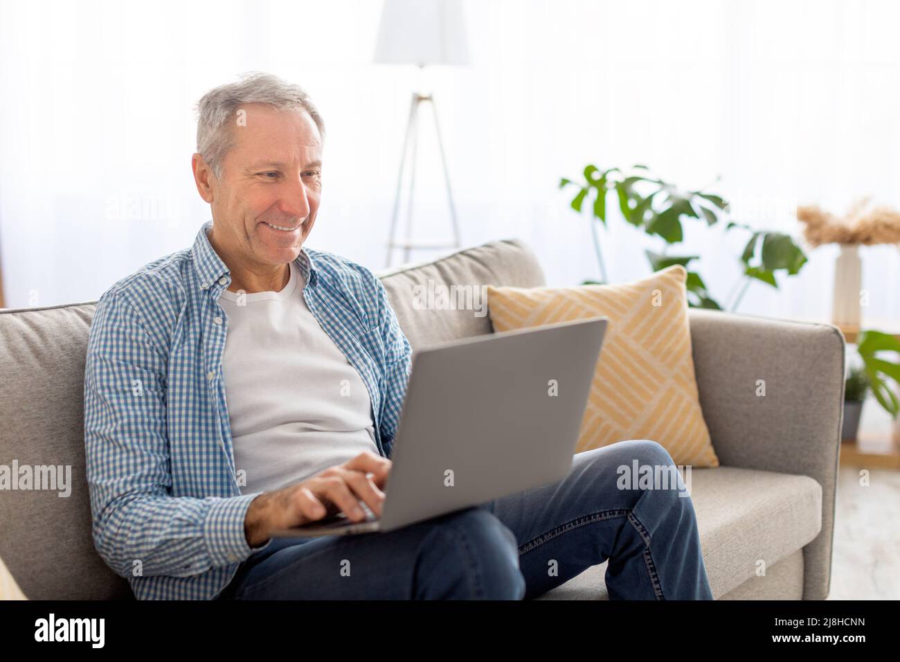 Confident casual mature using pc sitting on sofa Stock Photo