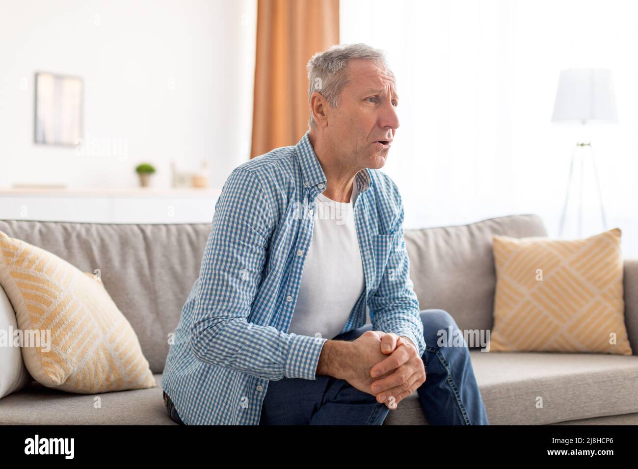 Mature man with knee pain sitting on couch at home Stock Photo - Alamy