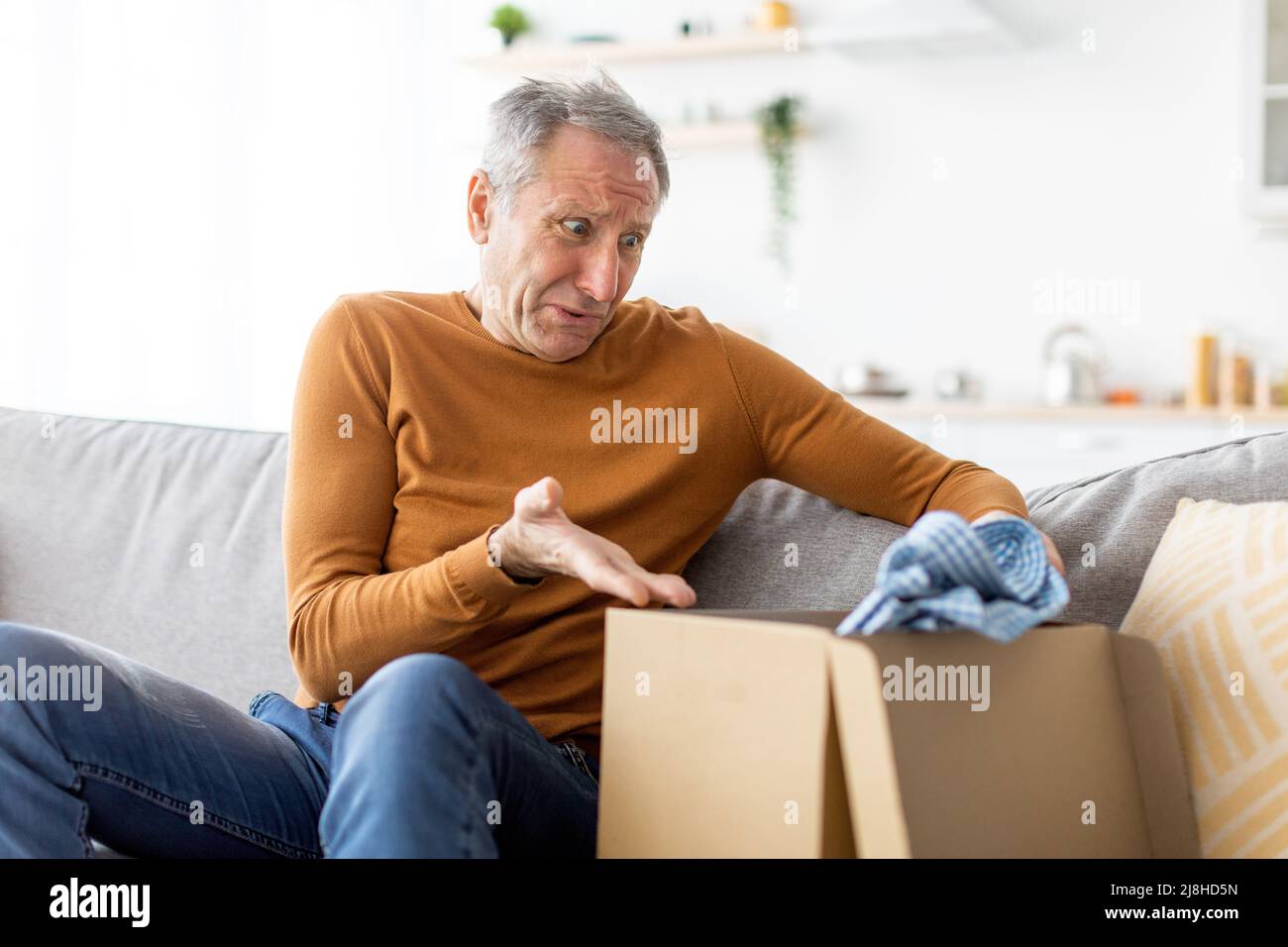 Sad mature man unpacking wrong parcel, delivery mistake Stock Photo