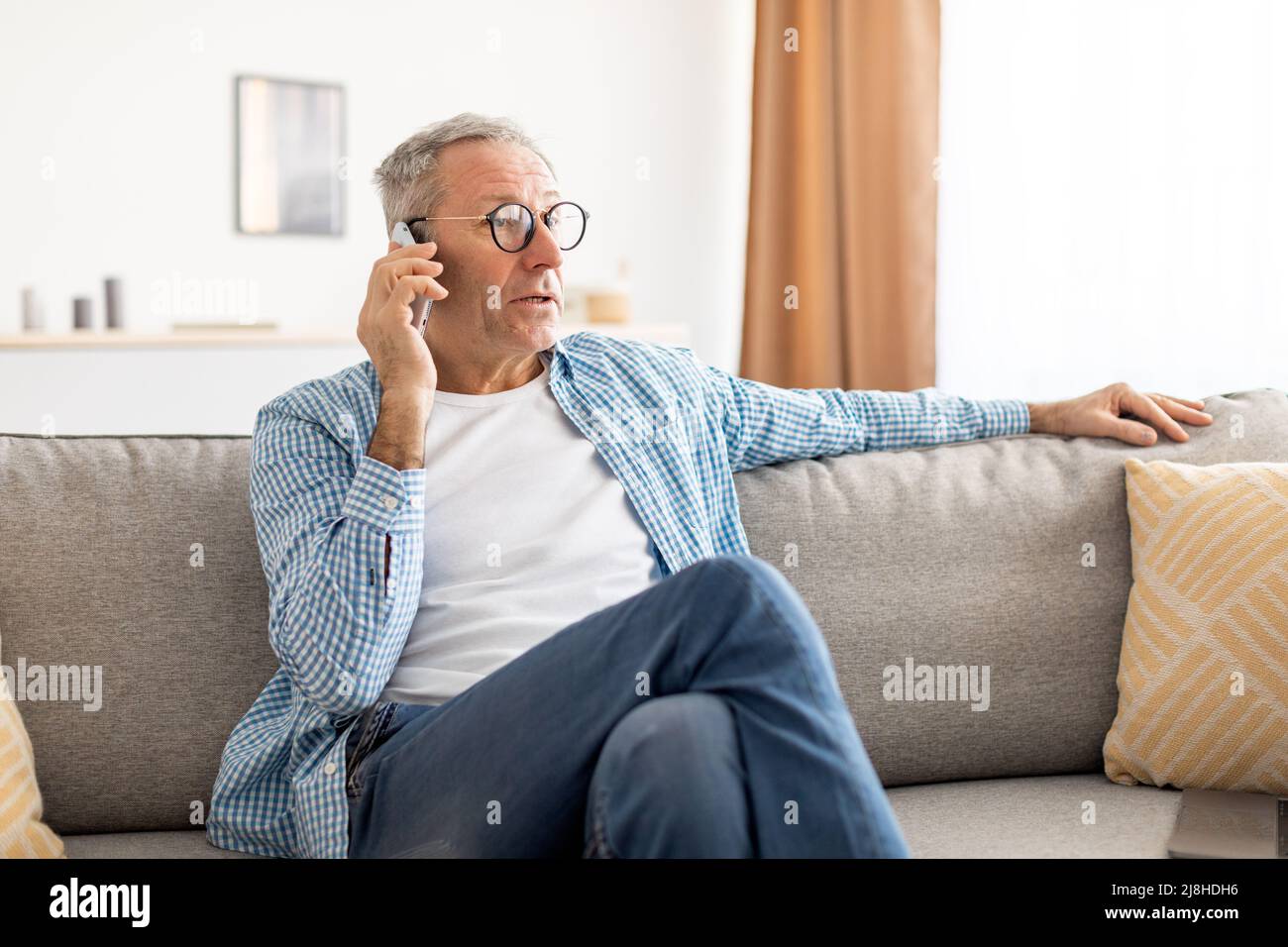 Mature man talking on cellphone sitting on couch Stock Photo