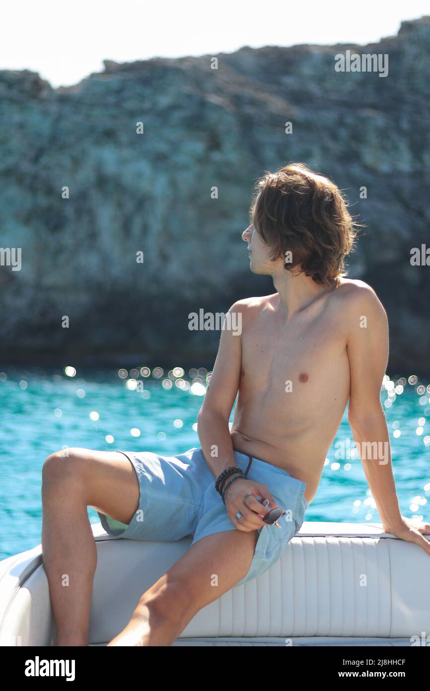 Handsome man enjoying freedom on Luxury yacht deck relaxing on high end boat summer vacation trip. long blonde hair and sun tanned body. Stock Photo