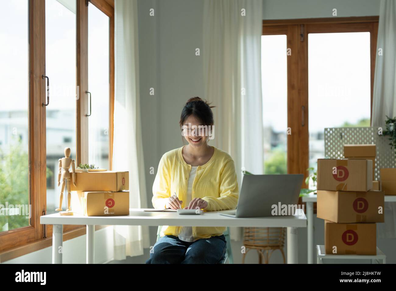 Close up asian female entrepreneur, checks online orders and uses a price calculator to calculate product prices and packs products into boxes to Stock Photo
