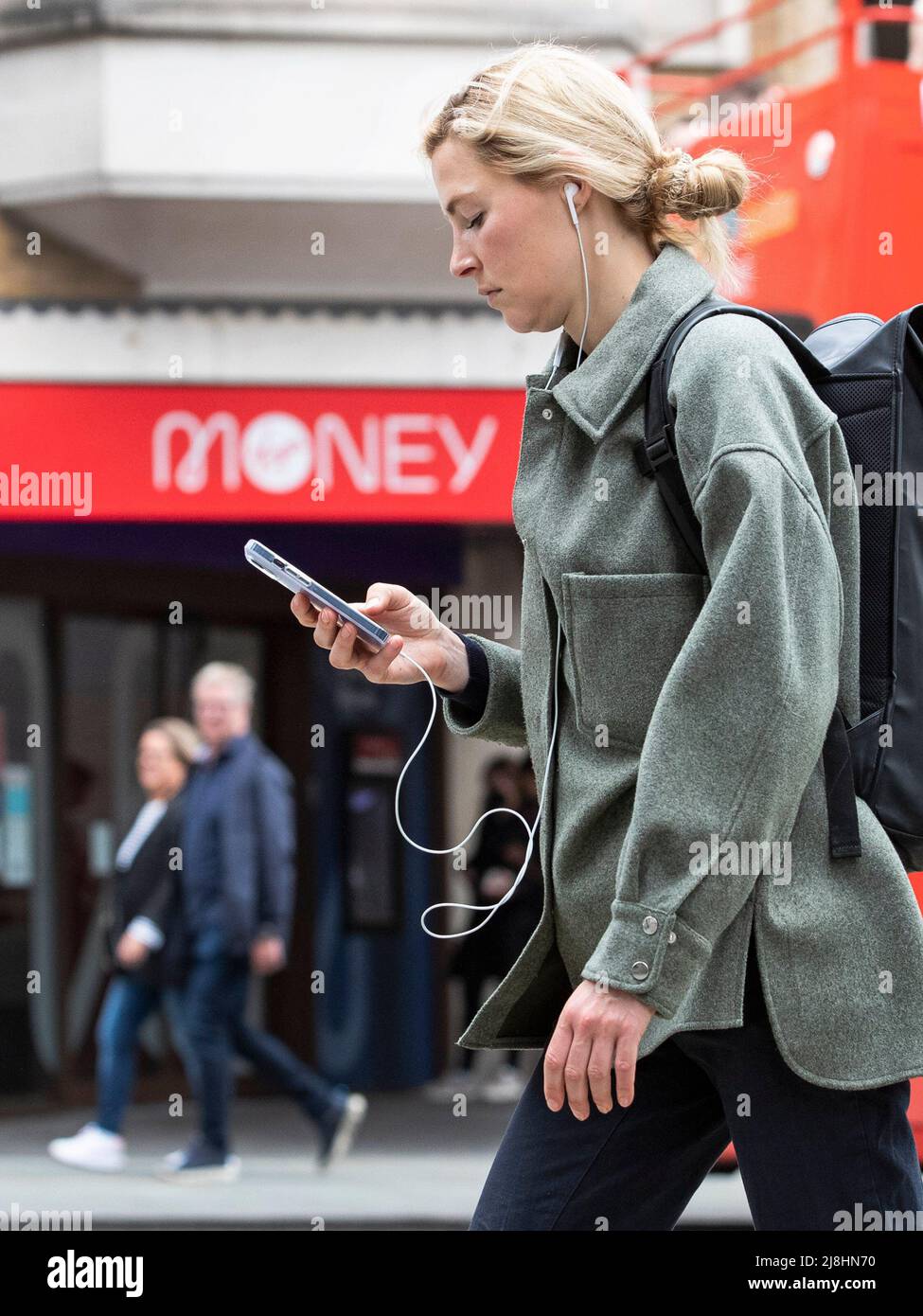 London - 16/05/2022. Credit: A woman looks at her phone as she walks past a Bank sign saying ‘Money’  in Central London as the cost of living crisis f Stock Photo