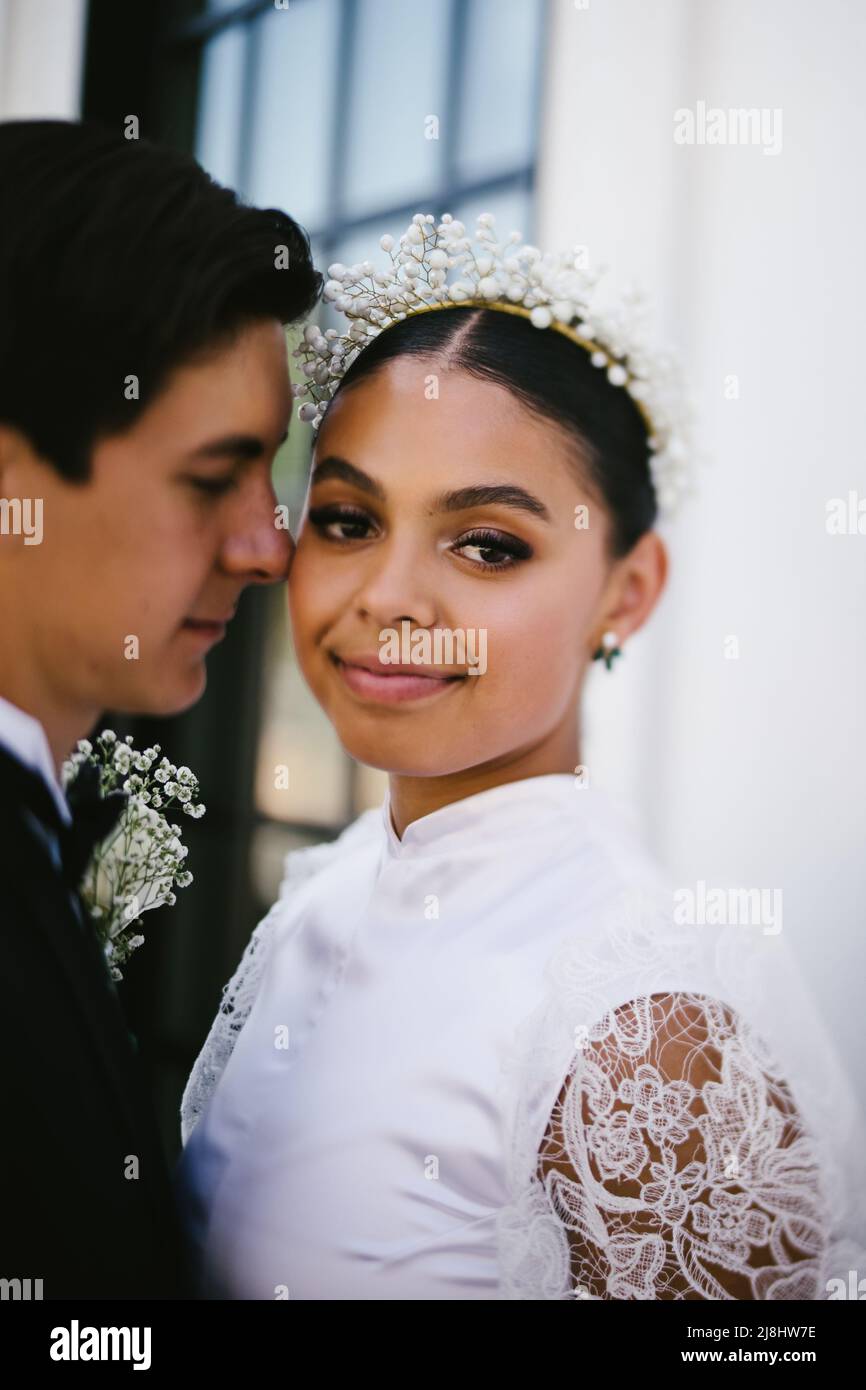 Latina bride makes eye contact while husband snuggles her Stock Photo
