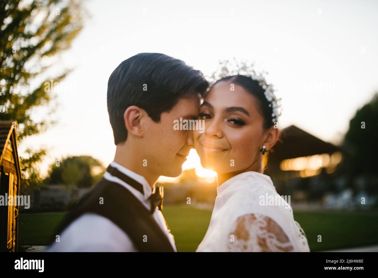 Bride and groom of mixed race snuggle in the sunset and golden light Stock Photo