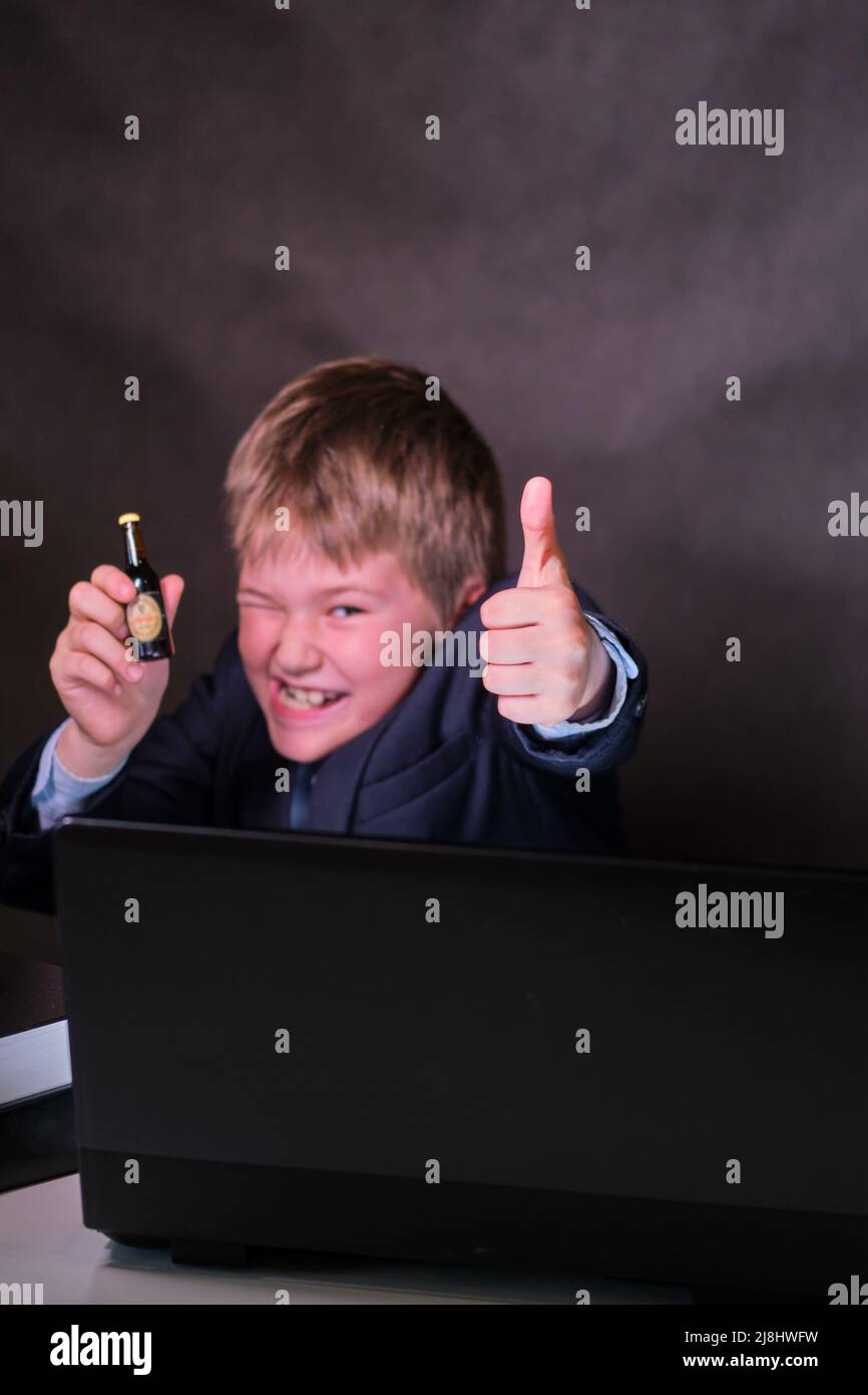 A happy boy in a school suit with a bottle of alcohol in his hands, copy space on a dark studio background Stock Photo