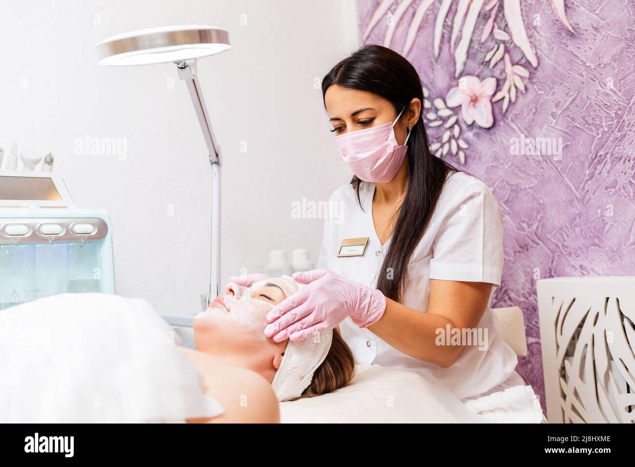 Worker at protective mask and medical gloves massages client's face. Concept of professional