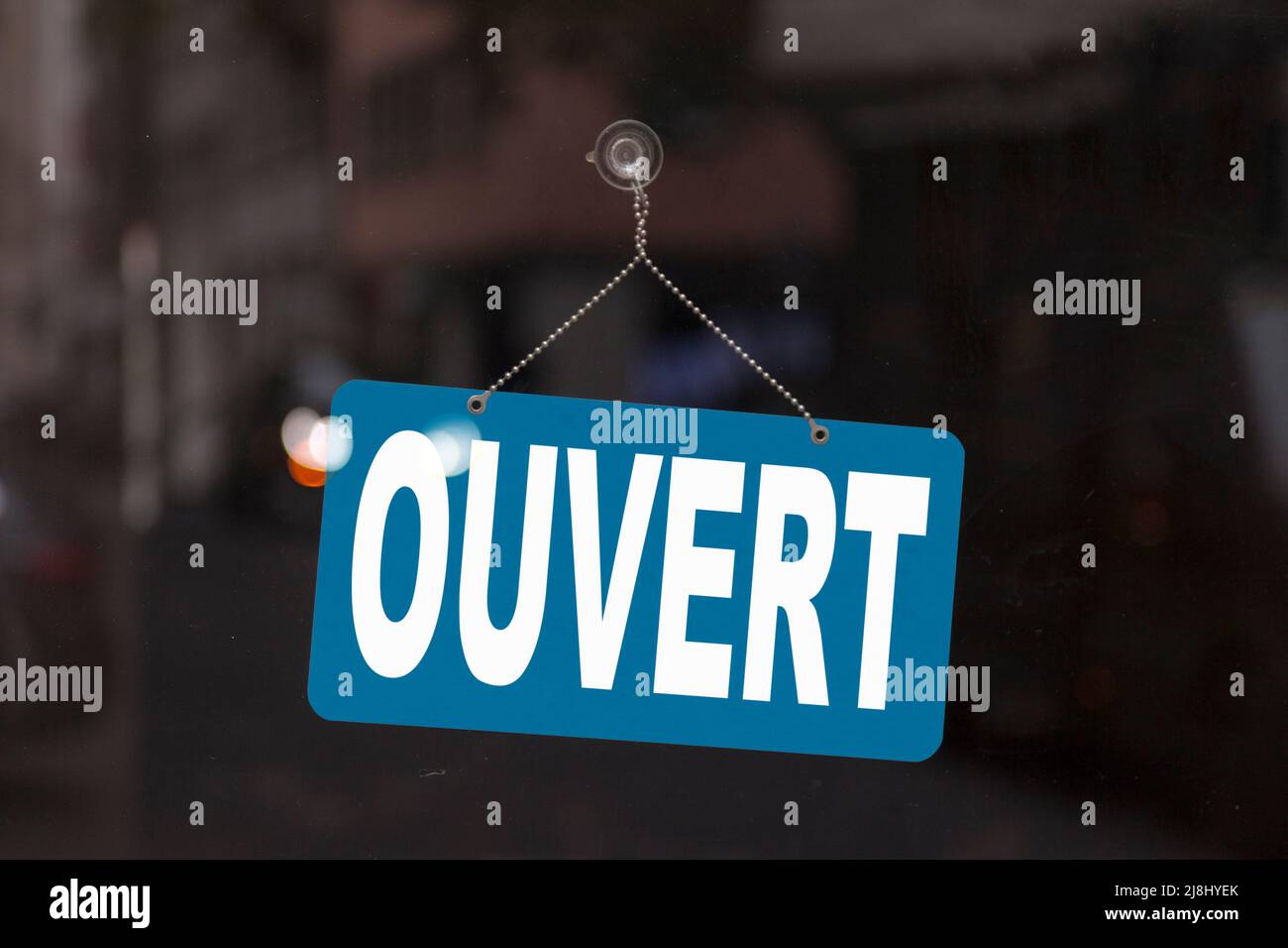 Close-up on a blue sign in the window of a shop displaying the message in French - Ouvert - meaning in English - Open -. Stock Photo