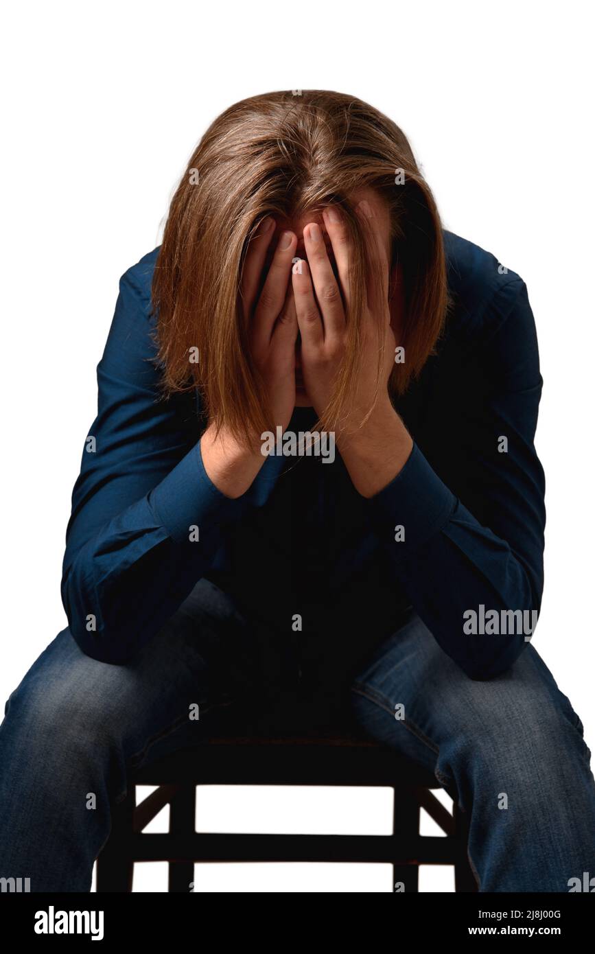Sad cheerless man hiding face with his hands sitting on chair isolated on white. Frustrated depressed young guy having troubles searching decision Stock Photo