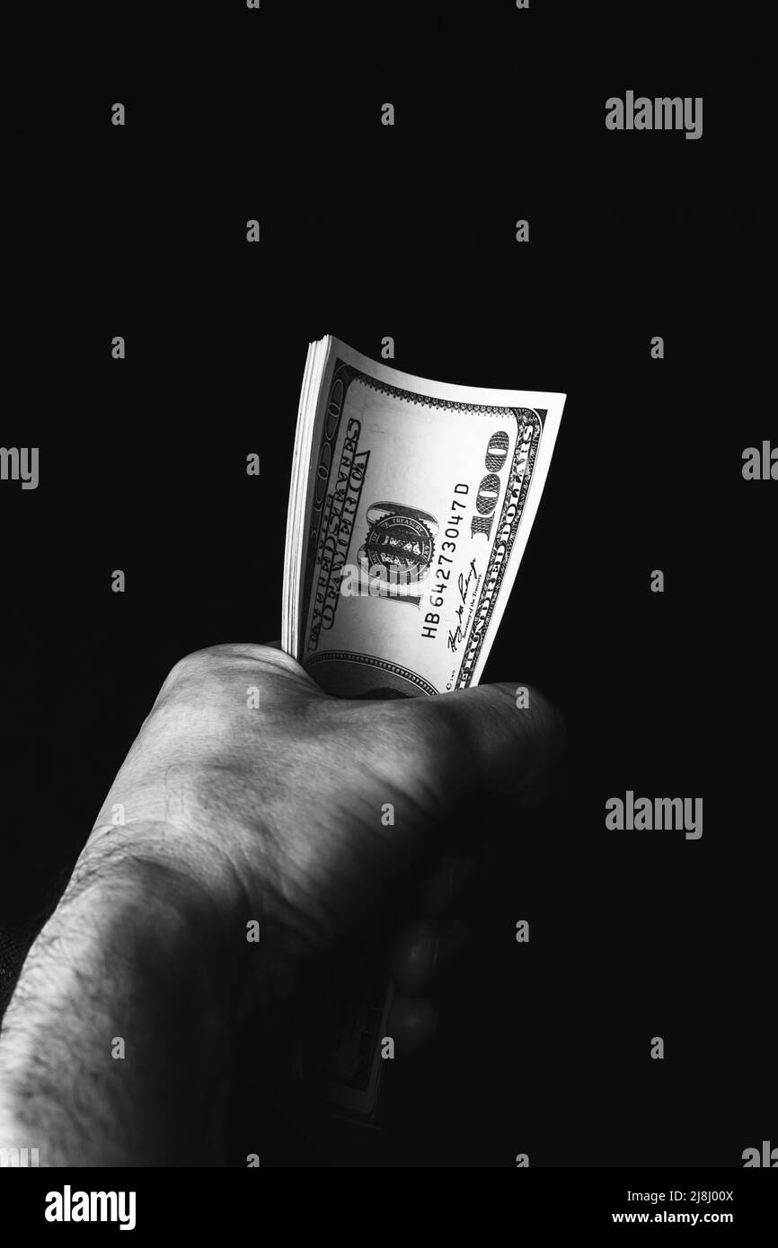 Male hand holding us hundred dollars banknotes on black background. Man with american money closeup. Black and white photo Stock Photo