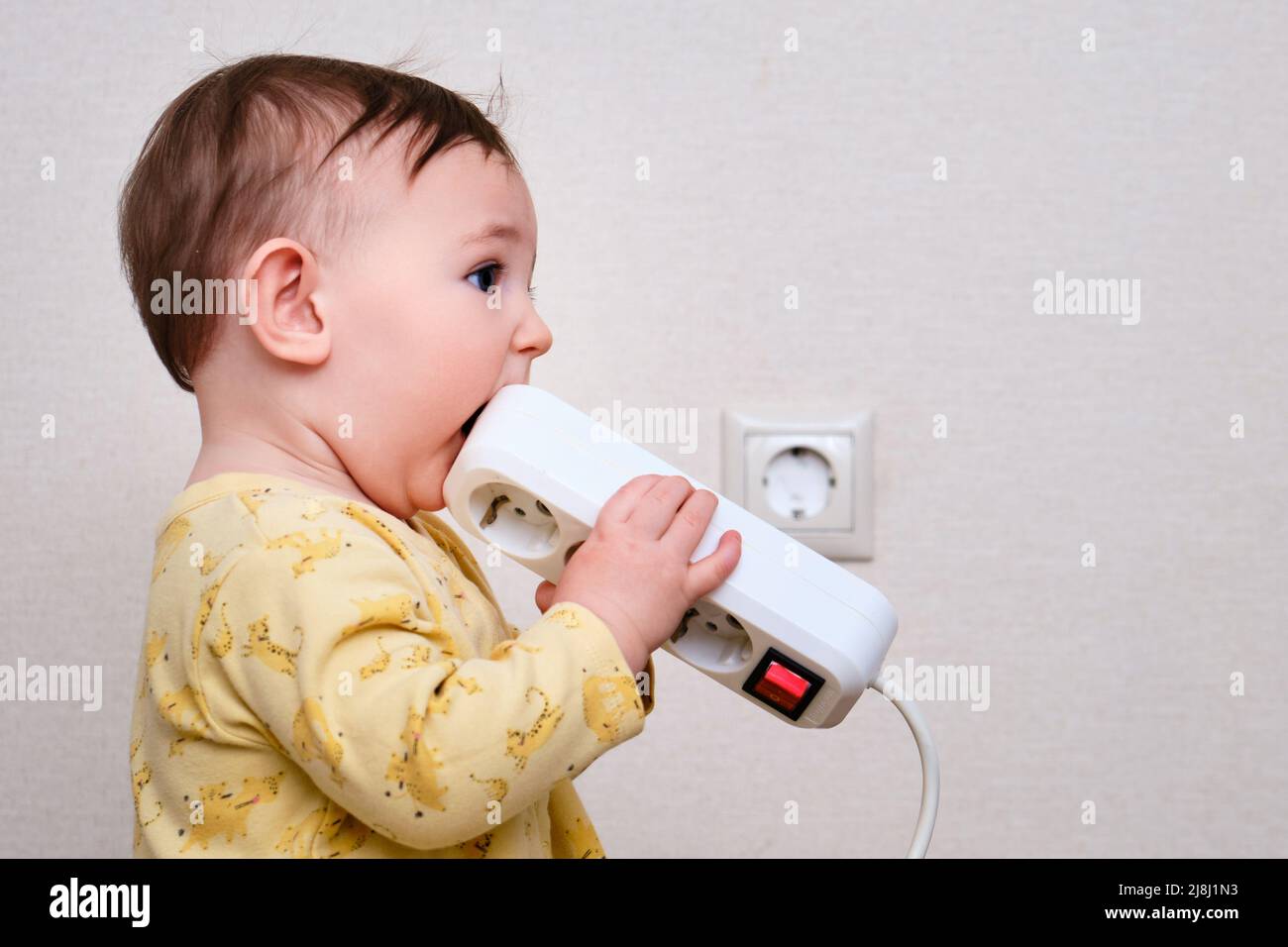 Toddler baby boy gnaws electrical wires while sitting on the floor