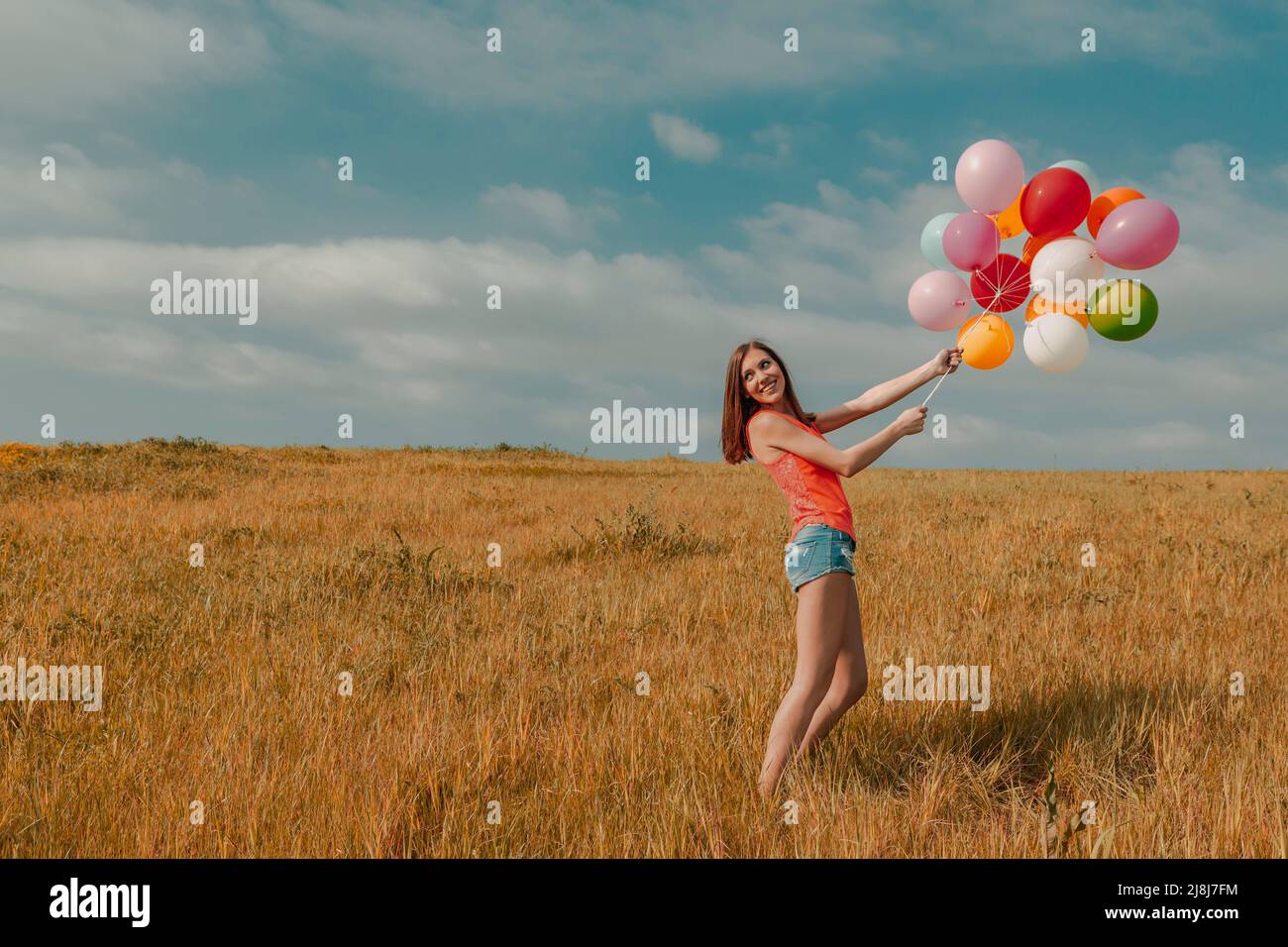 Young woman in the field holding colorful balloons Stock Photo