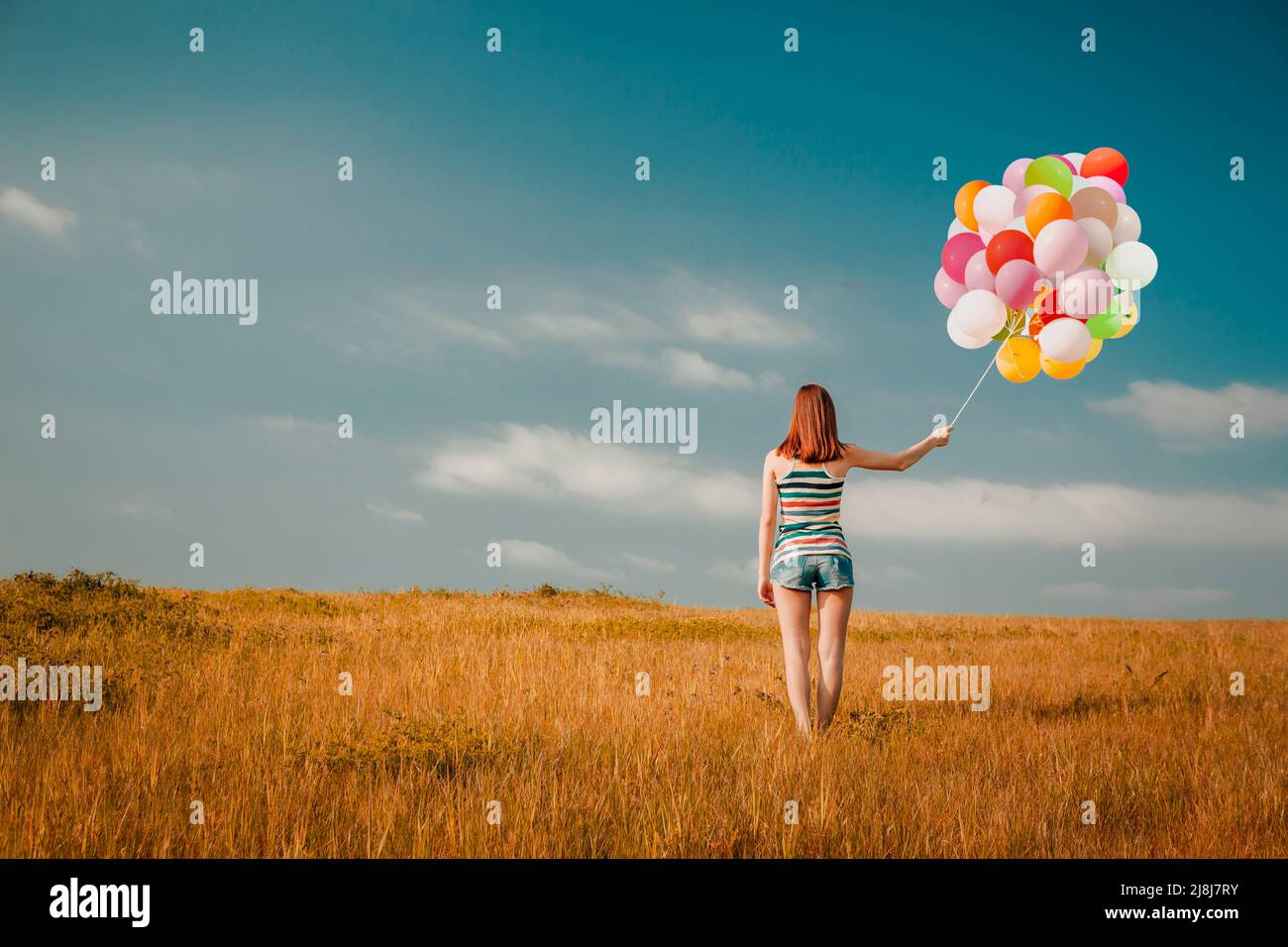 Young woman in the field holding colorful balloons Stock Photo