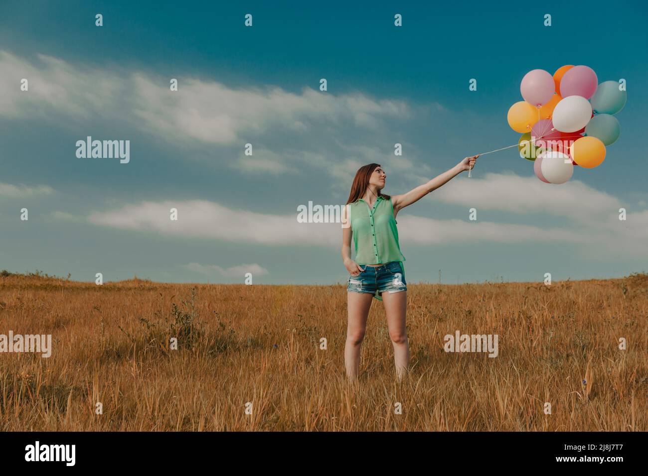 Beautiful young woman walking on meadow holding ballons Stock Photo