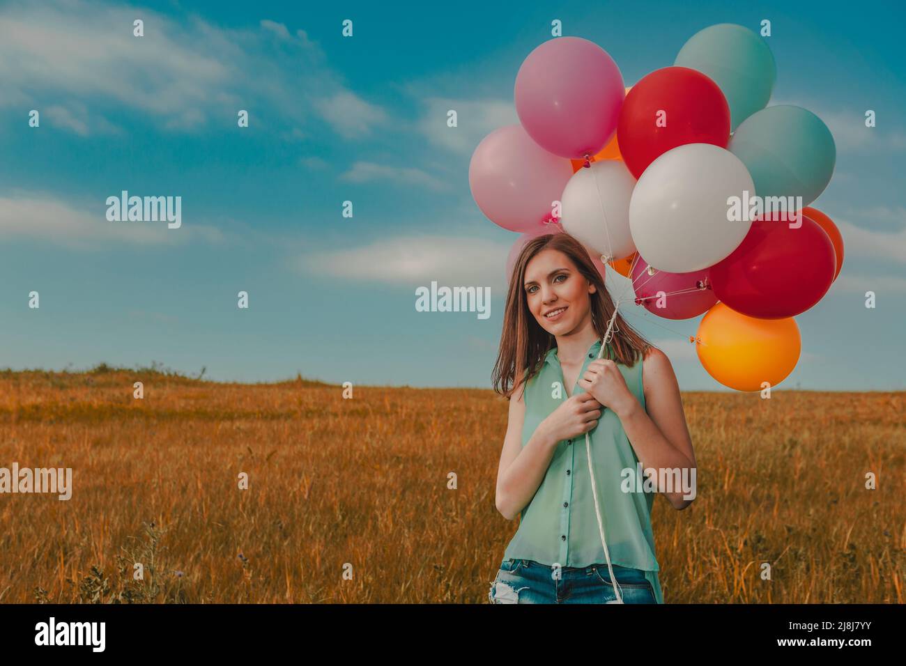 Young beautiful woman with colorful balloons on a green meadow Stock Photo