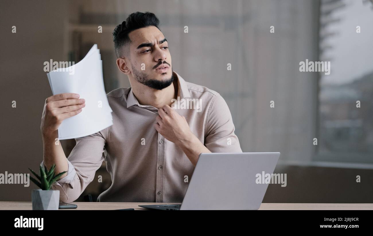 Hispanic exhausted male business man annoyed guy suffer from summer heat in office home without air conditioner feeling hot high air temperature Stock Photo