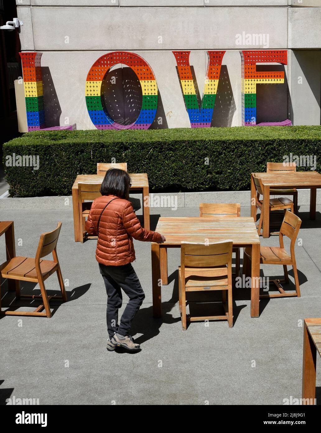 A woman enjoys a quiet courtyard space in San Francisco, California, with a sculpture titled 'Rainbow LOVE' by Laura Kimpton. Stock Photo