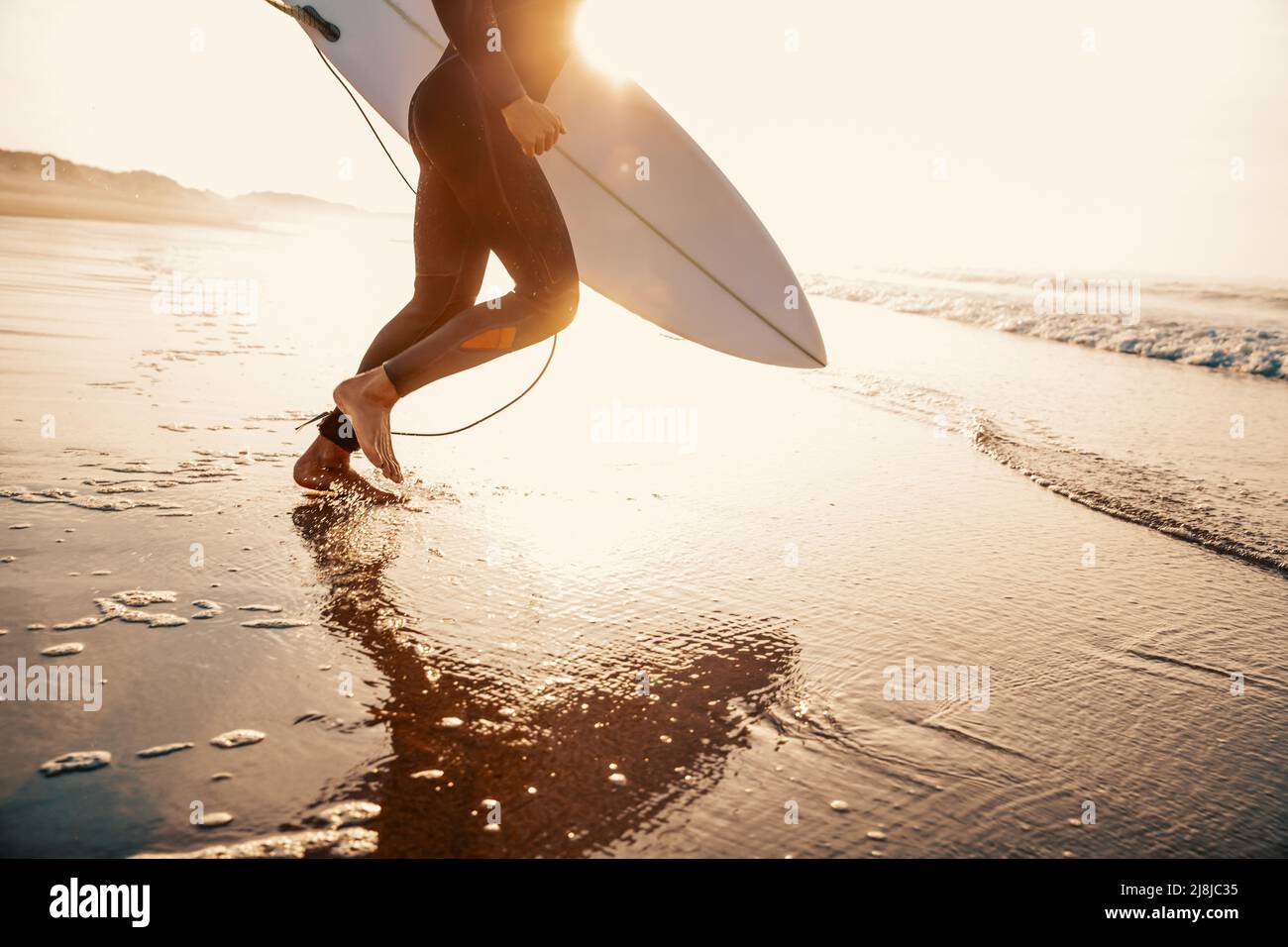 A surfer with his surfboard running to the waves Stock Photo