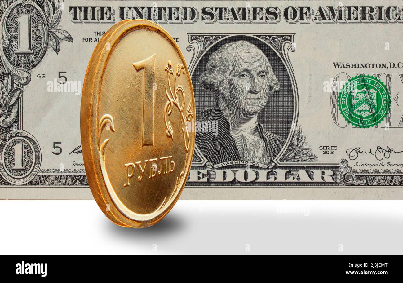 One rouble golden coin coin stands on the edge with a big dollar bill in the background. Image isolated on white background. Stock Photo