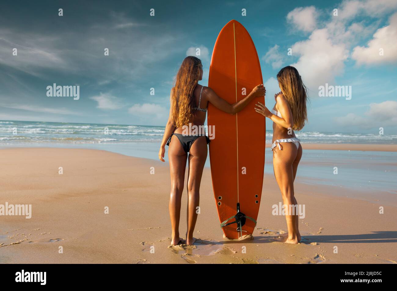 Best friends enjoying the summer, posing with a surfboard on the beach Stock Photo