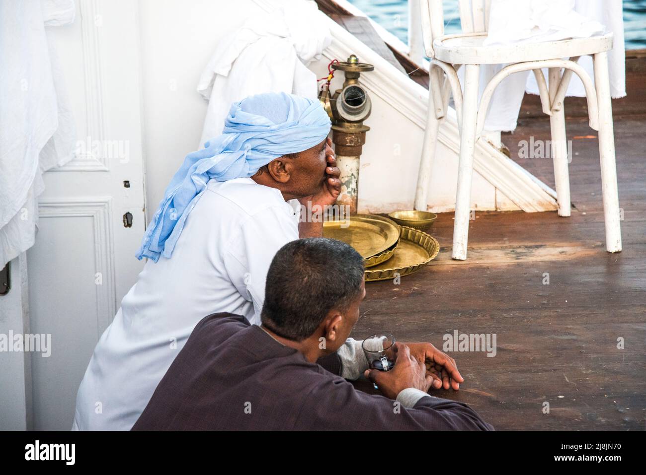 two crew members on a Nile Dahabiya tourist boat relax with coffee on the deck of the boat Stock Photo