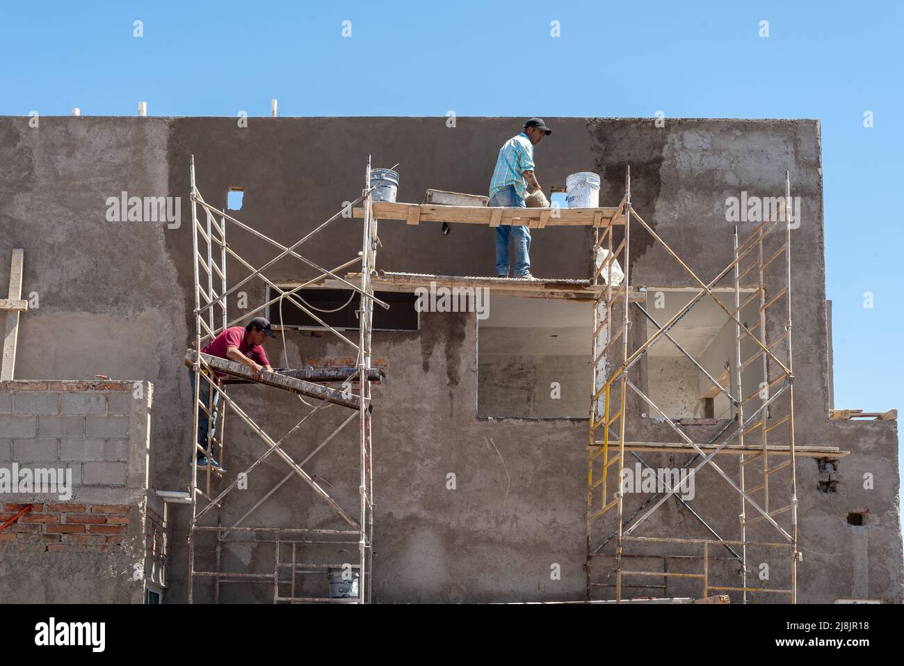Construction workers on metal scaffolding with wooden planks apply stucco on new building, San Carlos, Sonora, Mexico, United States. Stock Photo
