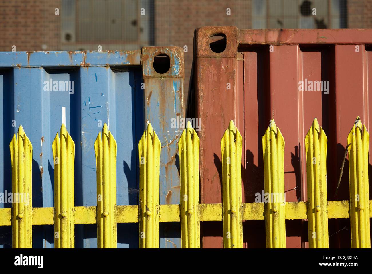 Red and blue container behind steel yellow painted fencing at Bullham Marine, Barking Stock Photo