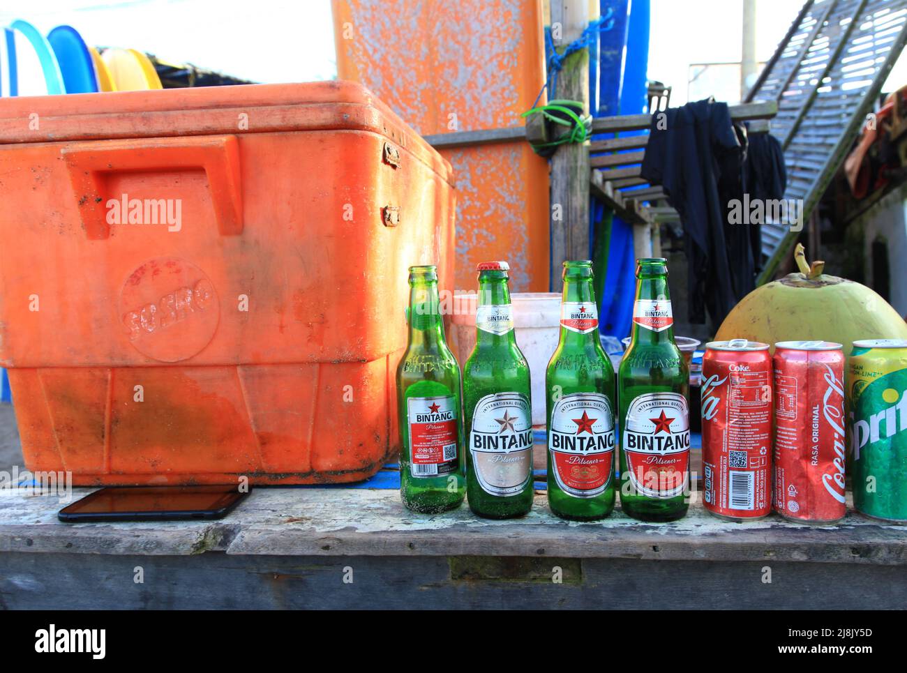 A beach bar in Canggu, Bali, Indonesia with an orange cooler box and several empties including local beer Bintang, Coca Cola and Sprite cans. Stock Photo