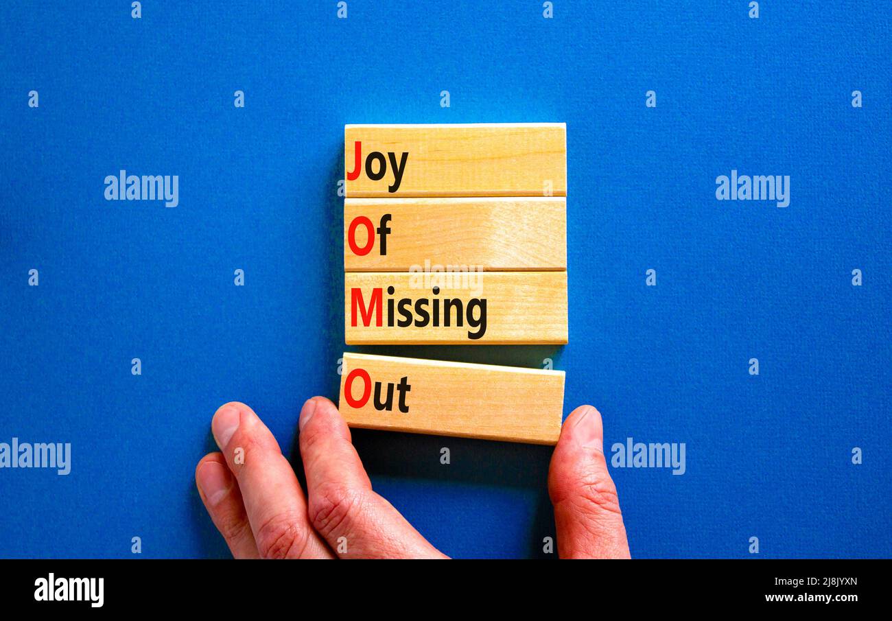 JOMO joy of missing out symbol. Concept words JOMO joy of missing out on wooden blocks on a beautiful blue background. Businessman hand. Business JOMO Stock Photo