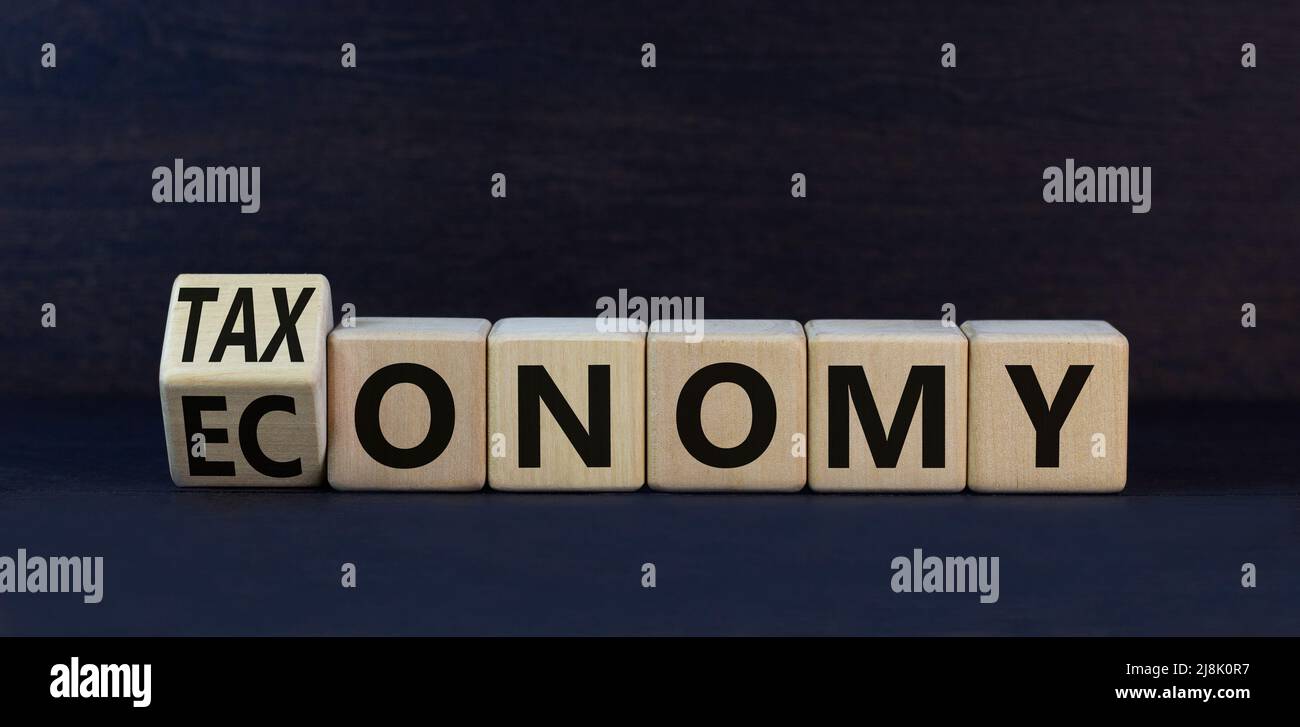 Taxonomy or economy symbol. Turned wooden cubes and change the concept word Economy to Taxonomy. Beautiful black table black background. Business ecol Stock Photo