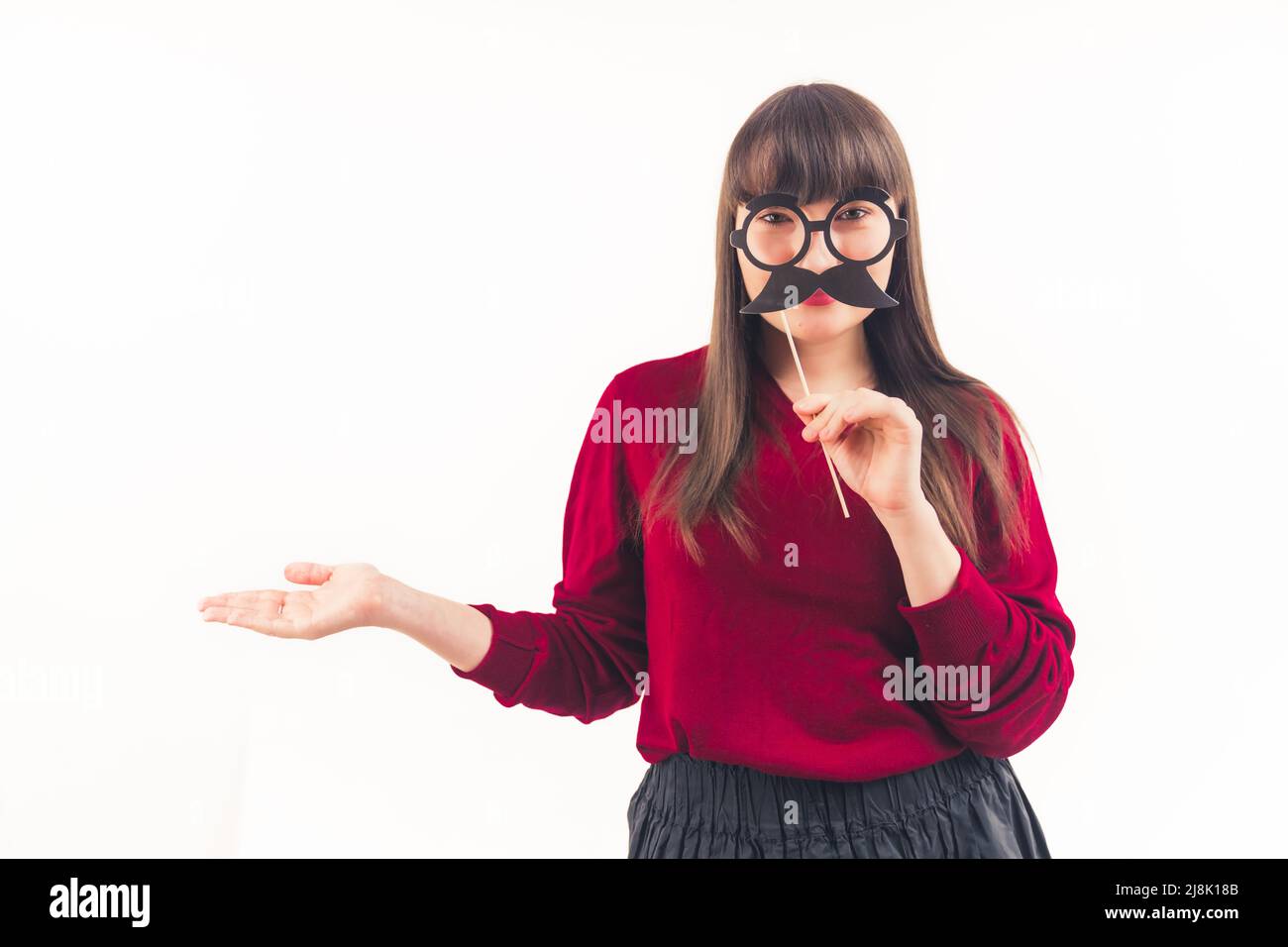 Dark-haired young woman holds fake moustache on a stick in front of her face and keeps her another hand open movember white background copy space isolated studio shot . High quality photo Stock Photo