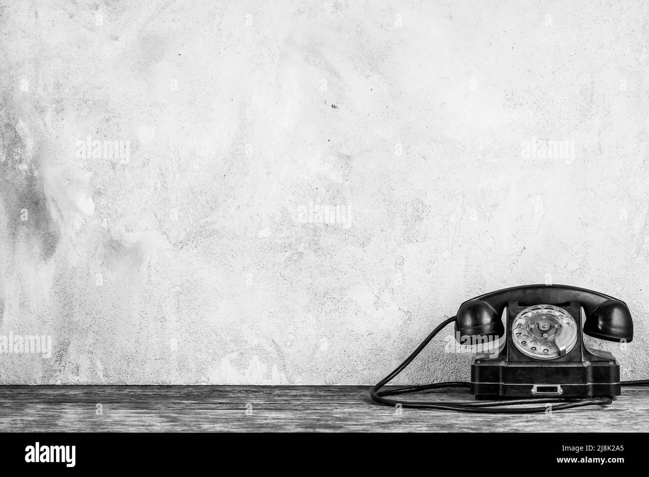 Retro black rotary telephone on wooden table in front gray concrete background Stock Photo