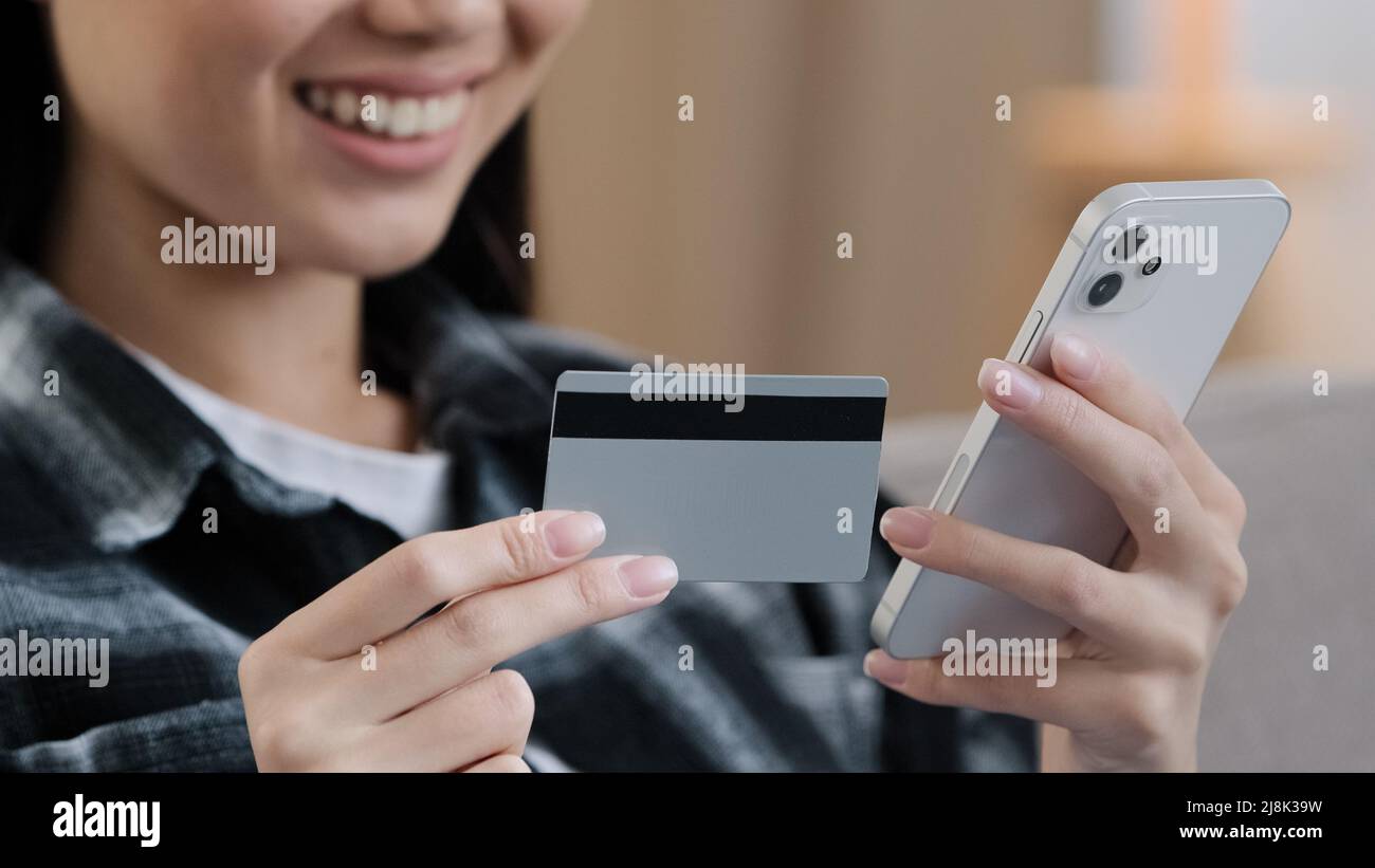 Close-up female hands unknown asian woman holding bank credit card mobile phone making online internet payments purchases e-commerce shopping order Stock Photo