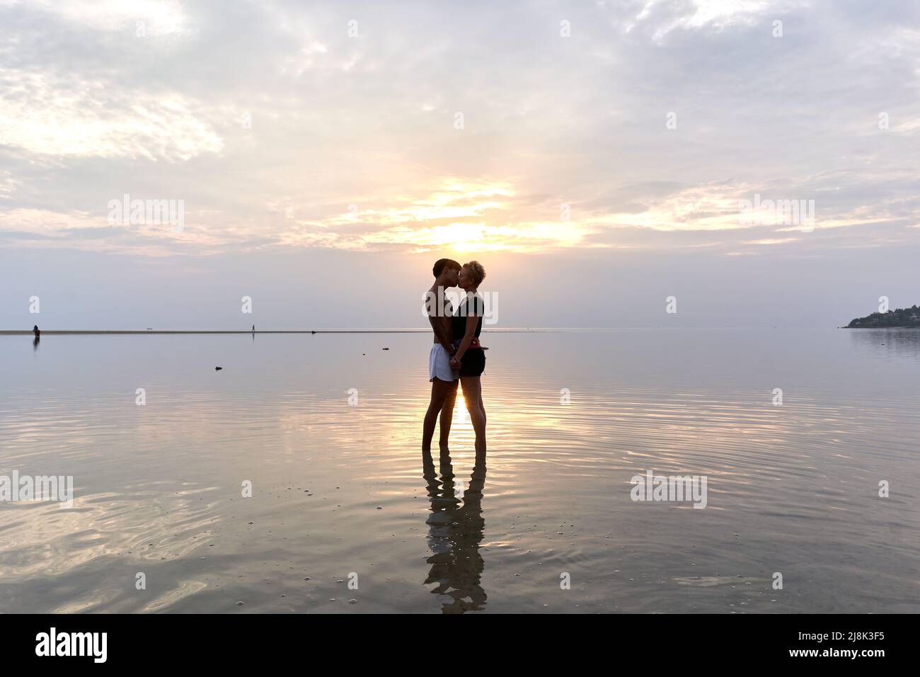 Silhouette of a couple kissing into the sea at sunset. Stock Photo