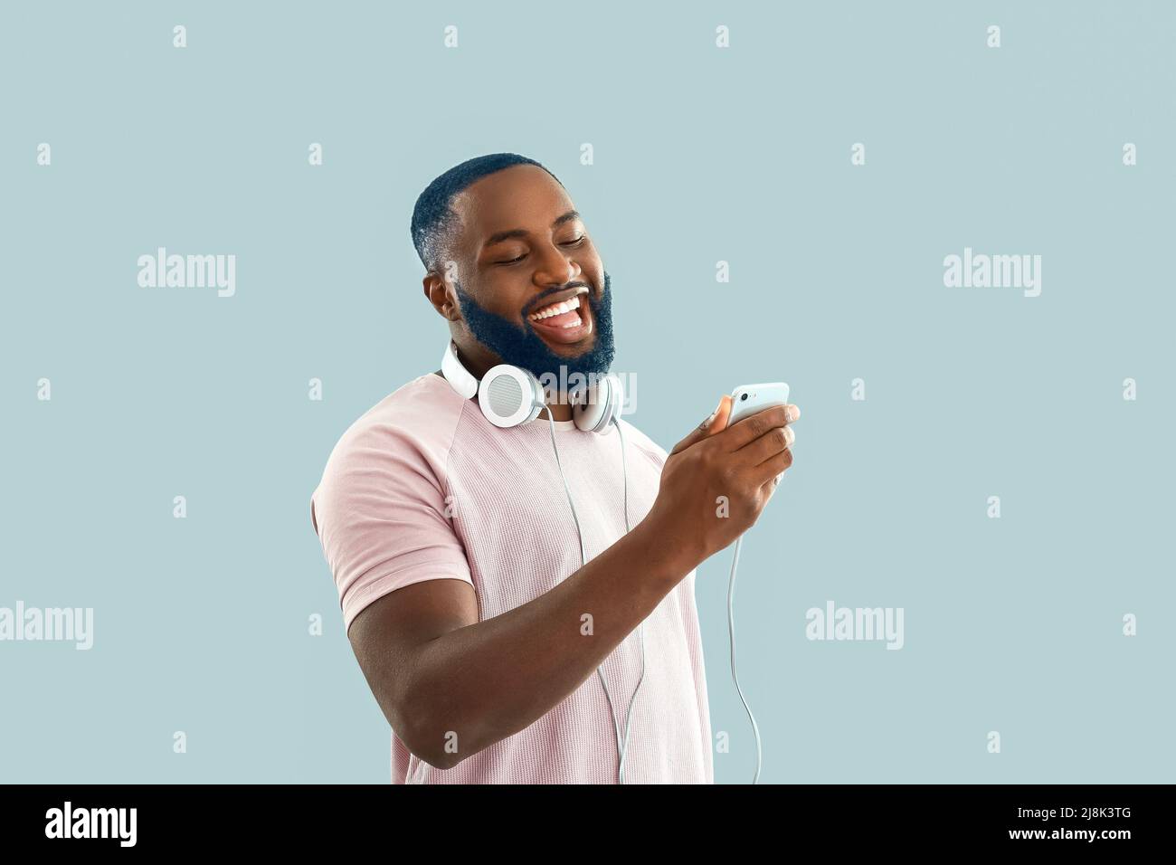 Happy African-American man with unusual color of hair and beard holding smartphone on light background Stock Photo