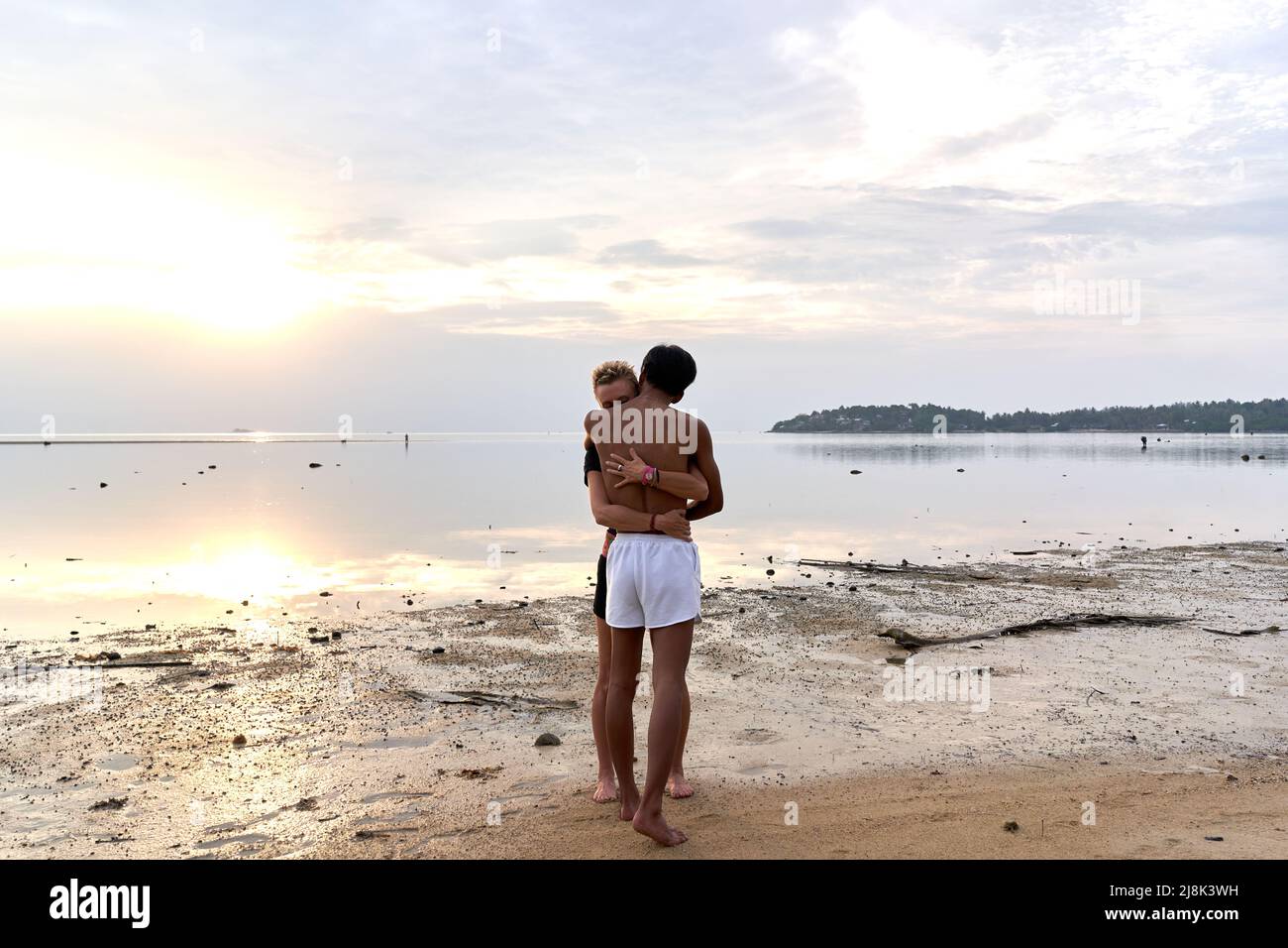 Multicultural couple embracing while standing next to the sea during sunset Stock Photo