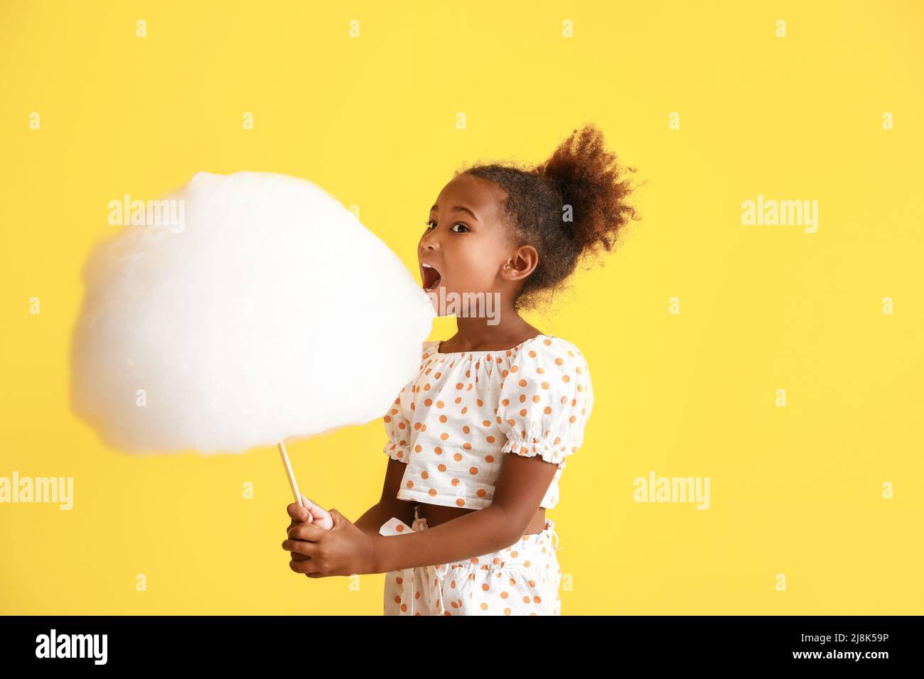 Little AfricanAmerican girl eating cotton candy on yellow background Stock Photo Alamy