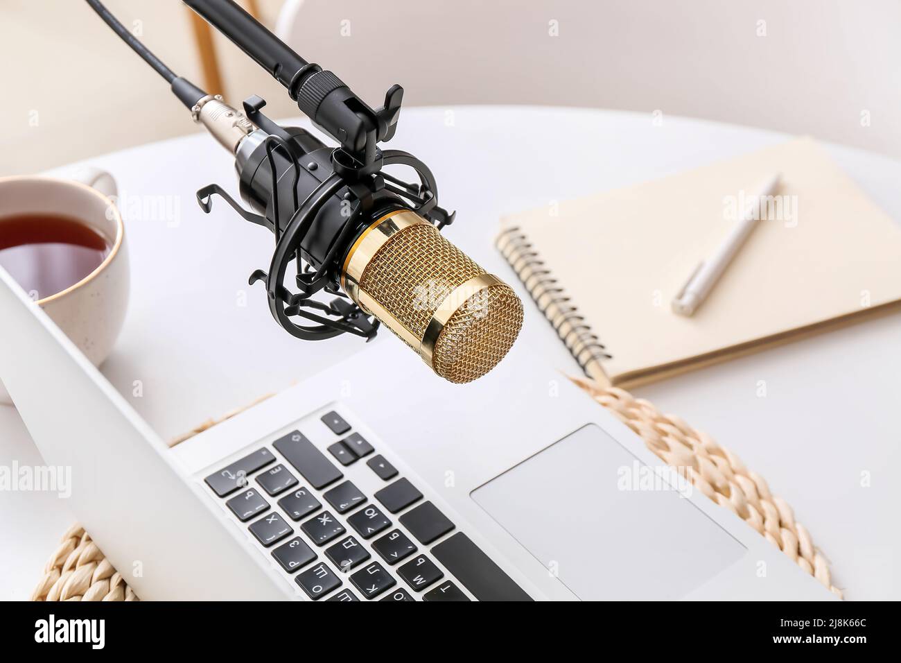 Stand with professional microphone, cup of tea and laptop on light table in room Stock Photo Alamy