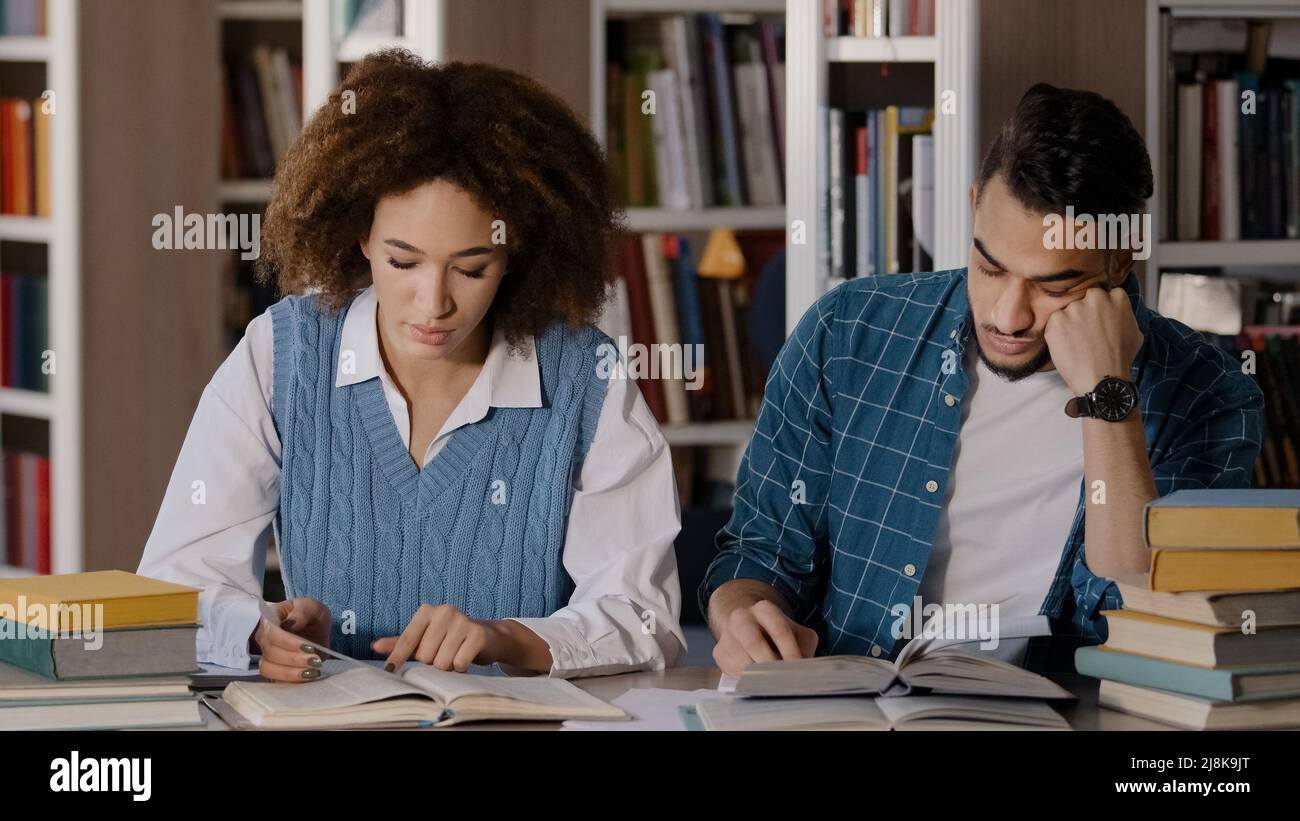 Two students guy and girl sitting at desk classroom writes notes in notebook writing information from textbook reading book young male student falls Stock Photo