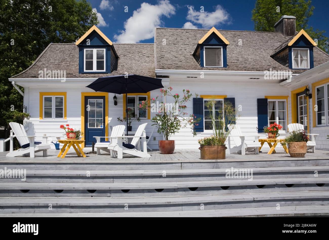 Back of old circa 1830 cottage style home with white wood plank cladding, cedar wood shingles roof and patio deck in summer. Stock Photo