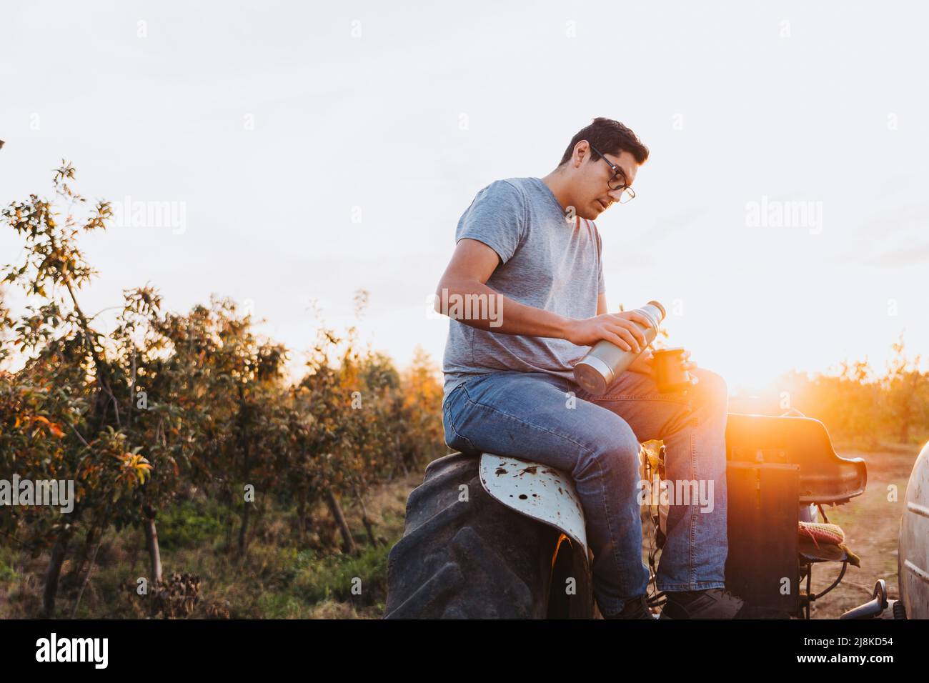 Young latin man drinking mate and relaxing, in a rural space, on top of an old little tractor. Hot beverage Stock Photo